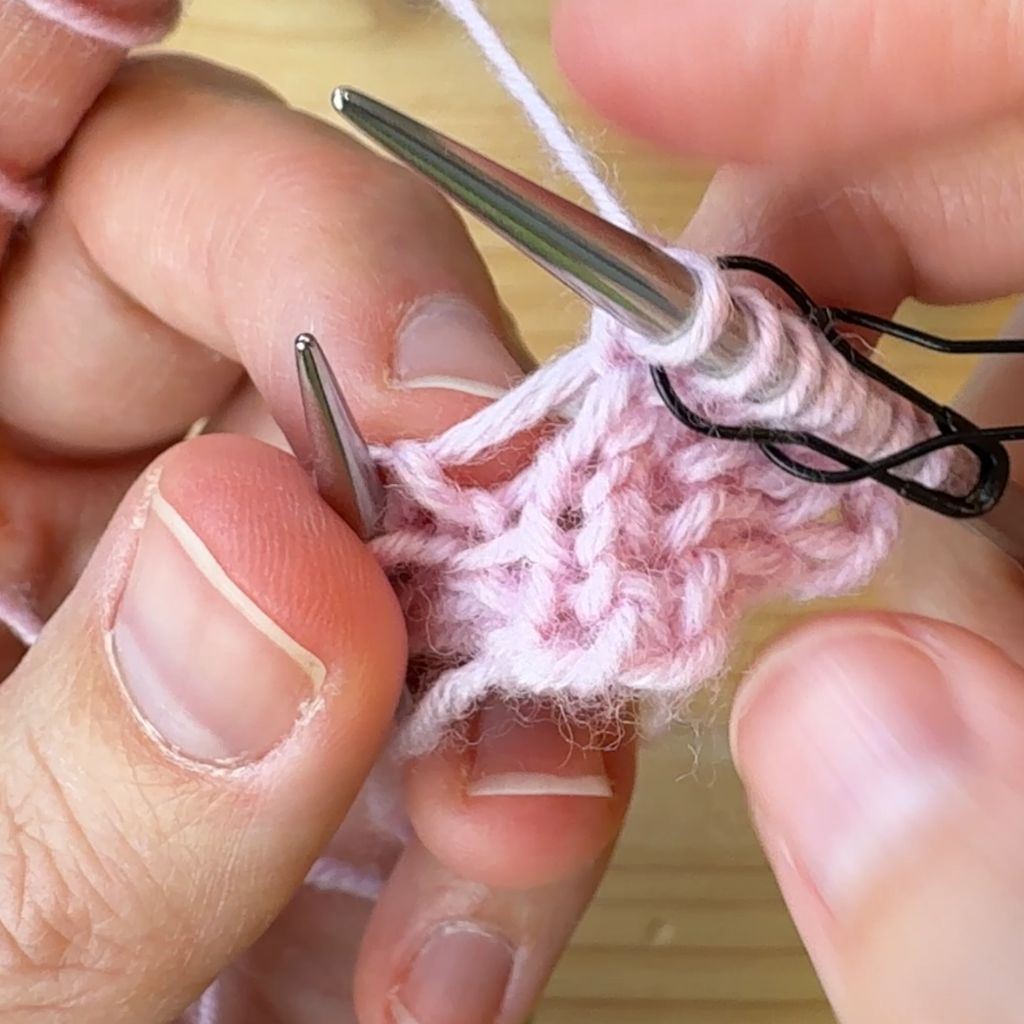 Linksgeneigte Zunahme stricken. Schritt 4.: Masche von der linken Nadel gleiten lassen. Die Masche neigt sich nach links.