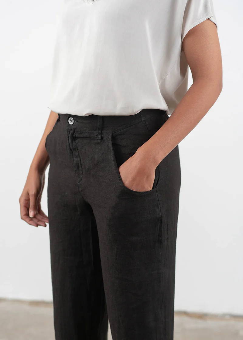 A close up image of a model wearing an off white short sleeved top with black linen trousers