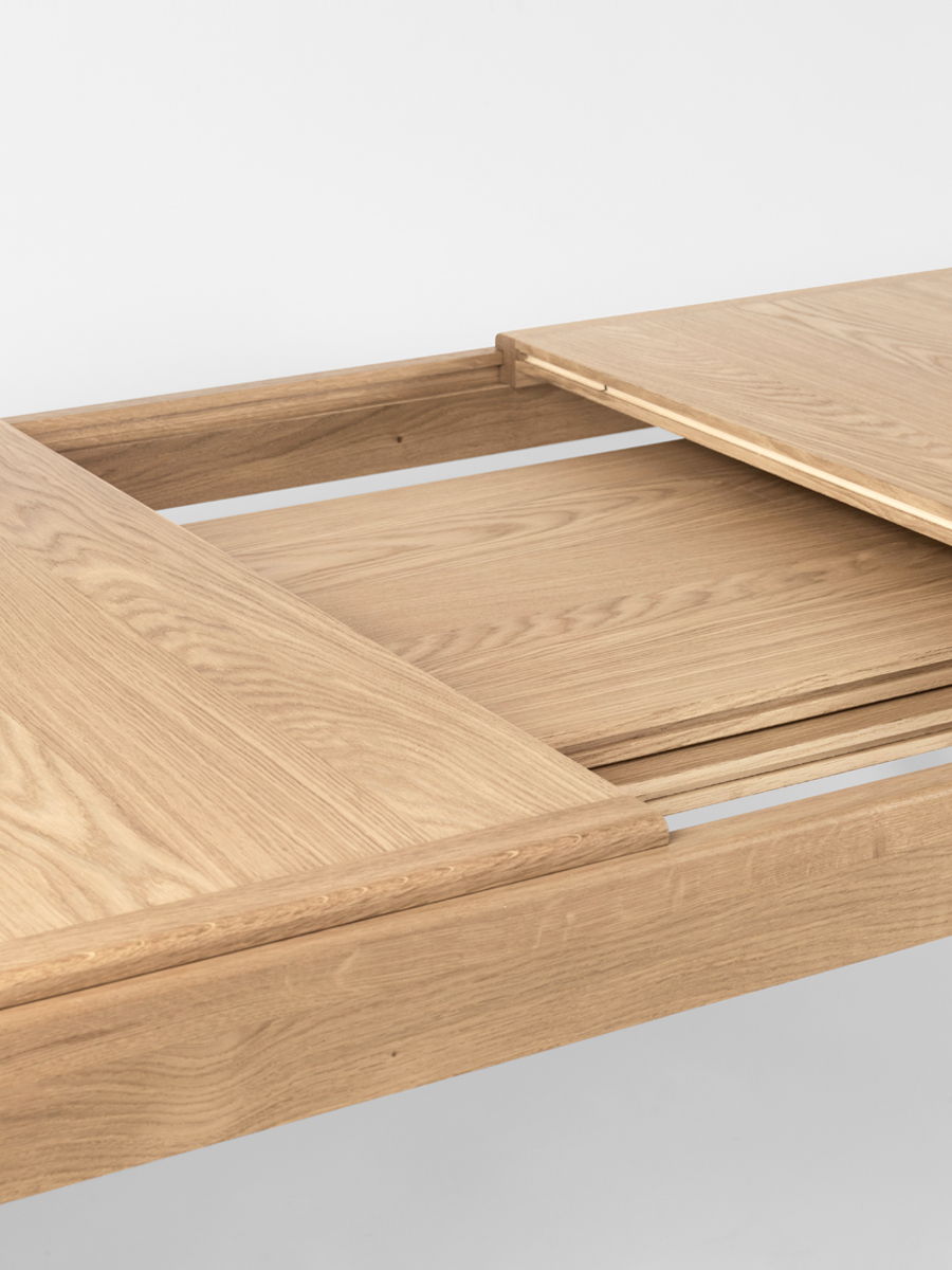 A wooden S-Extending dining table by Gubi with chairs, a coffee cup, and a magazine.