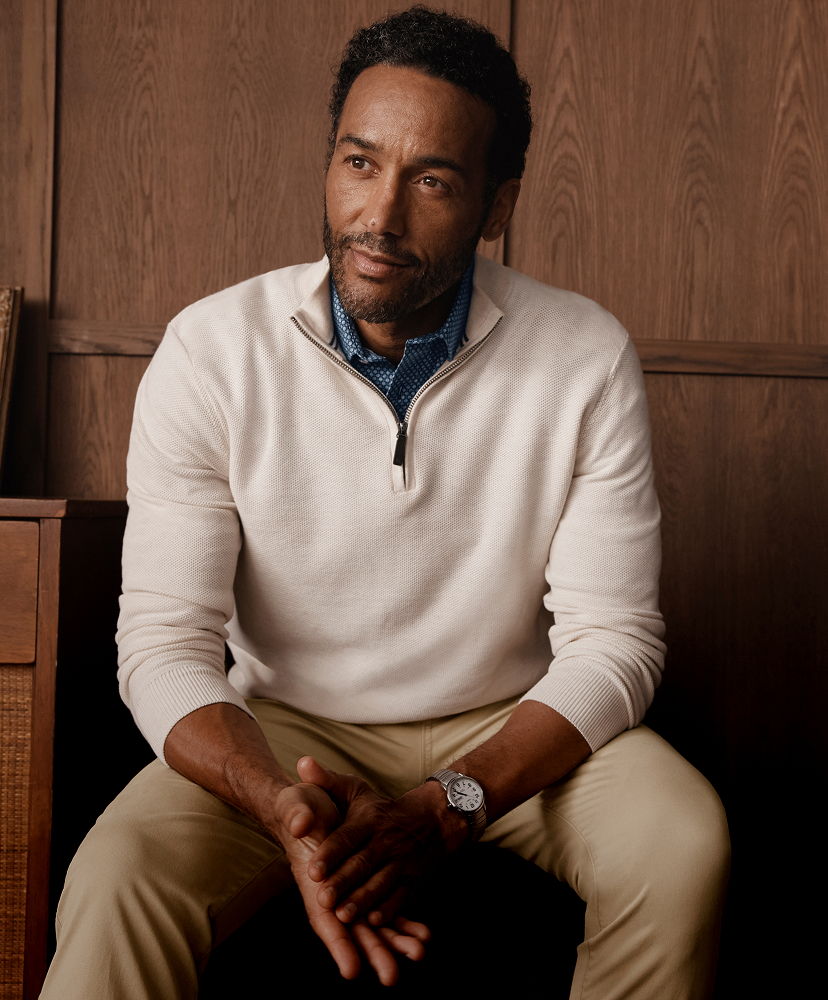 Man sitting casually, wearing a sweater and looking thoughtfully.