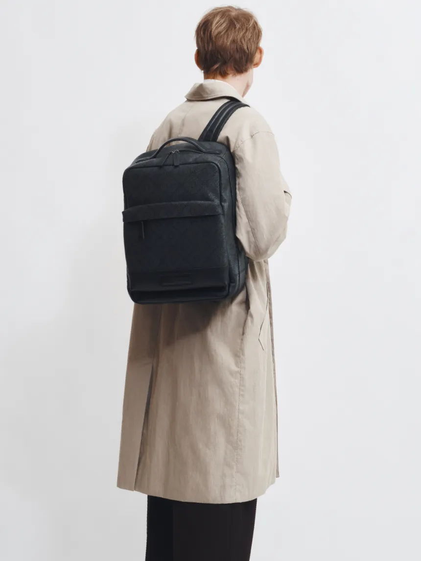 Person wearing a beige coat with a black backpack, facing away from the camera.