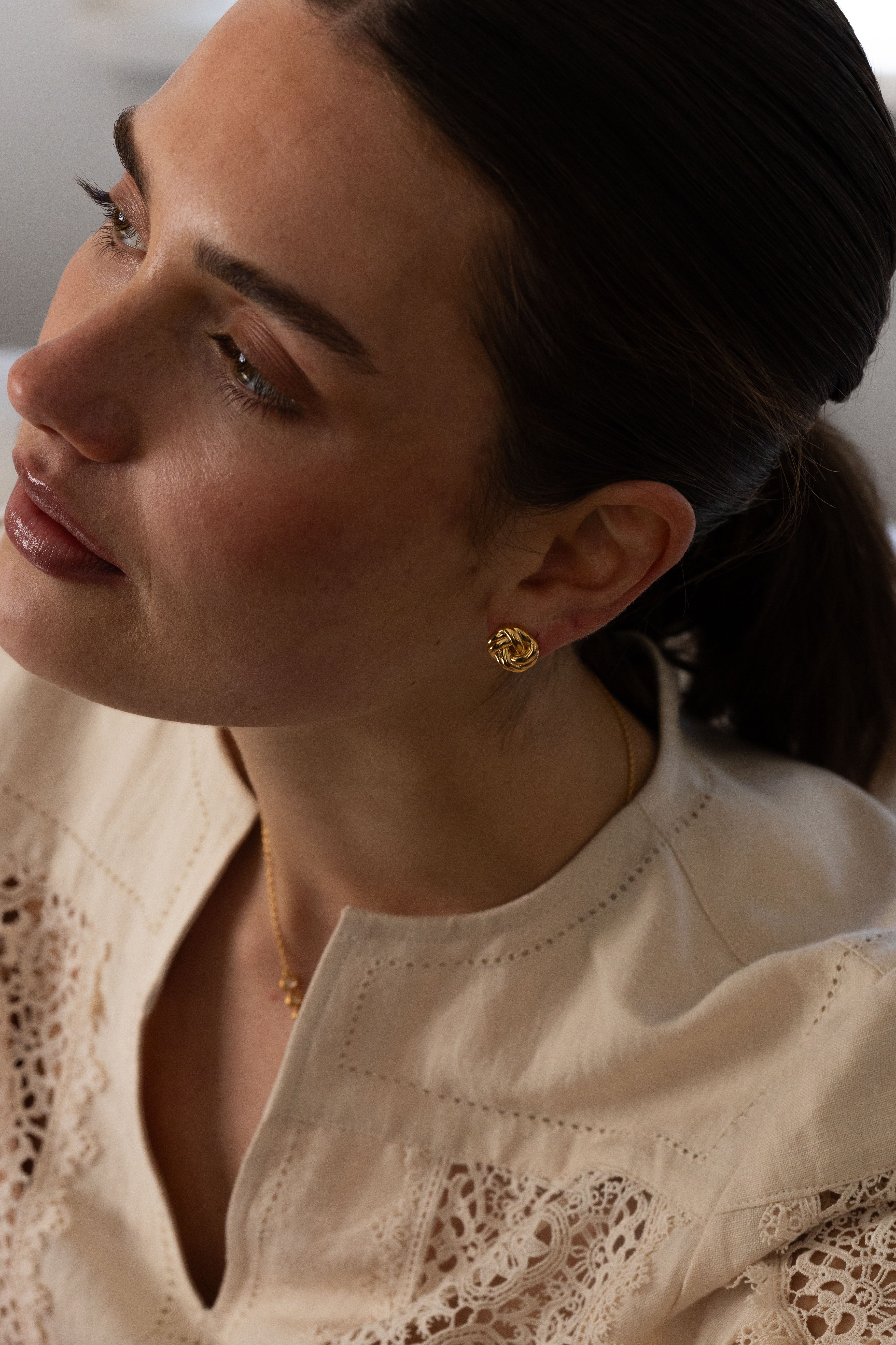 Woman with earrings gazing to the side, wearing a light-colored blouse.