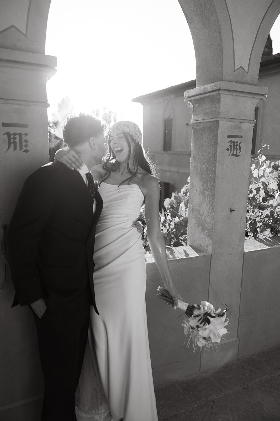 Couple embracing under an arch, dressed in formal wedding attire.