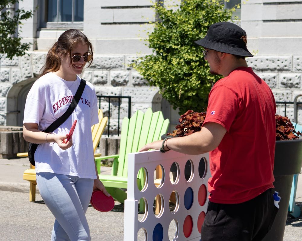 Two people playing a giant connect four game outdoors.