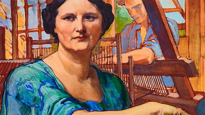 A woman in a blue dress poses in an artistic setting with a loom.