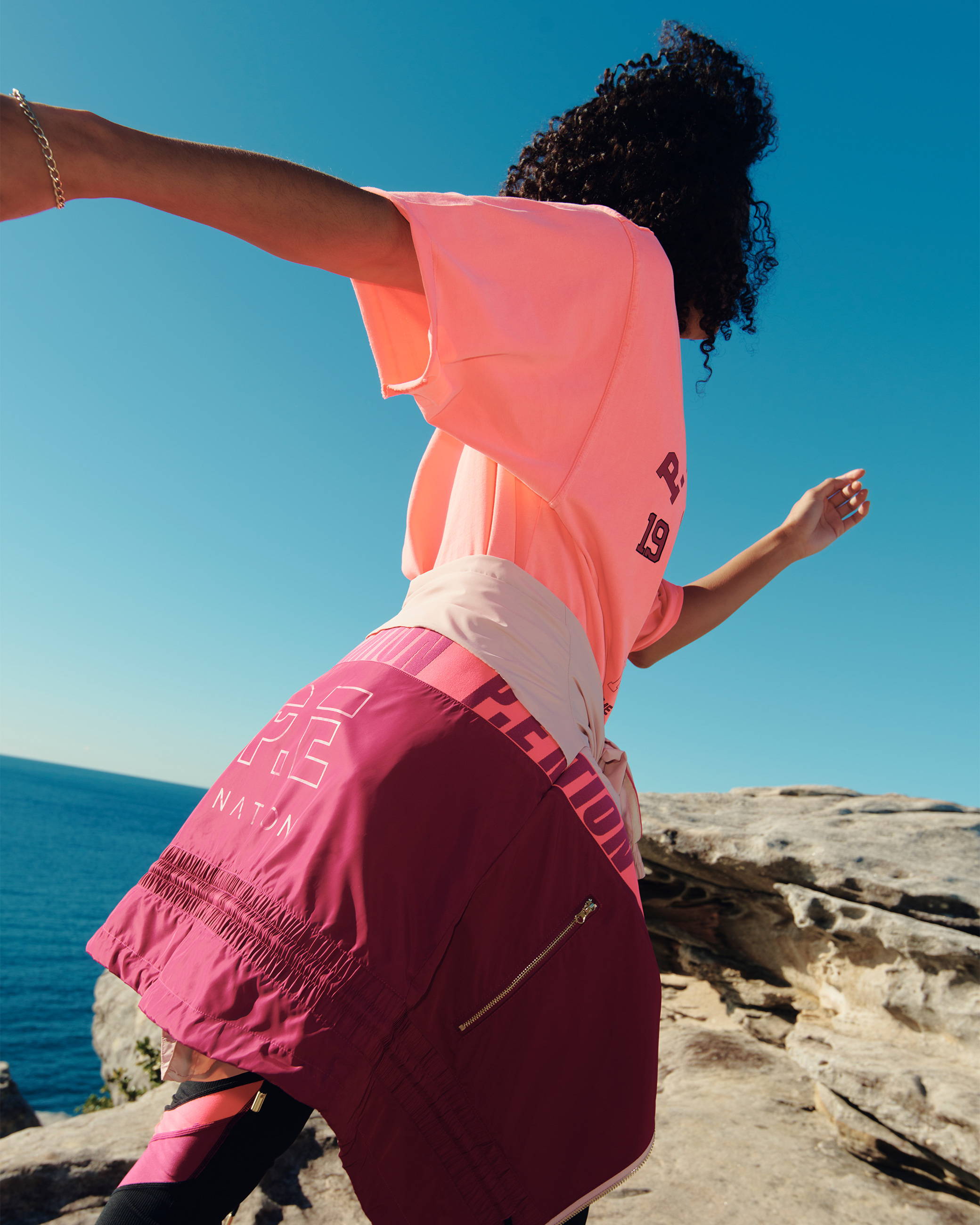 A girl jumping and running along the clifftops in Sydney. She is next to the ocean and wearing P.E Nation activewear