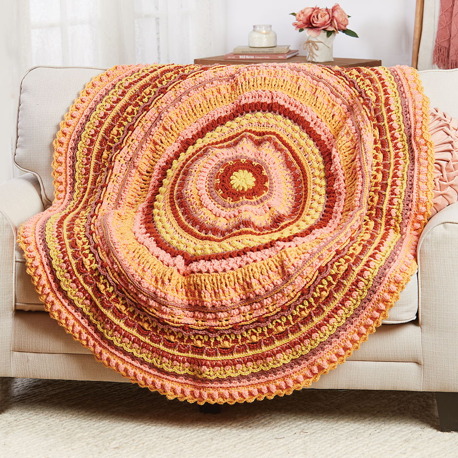Colorful circular crochet blanket draped over a beige couch.