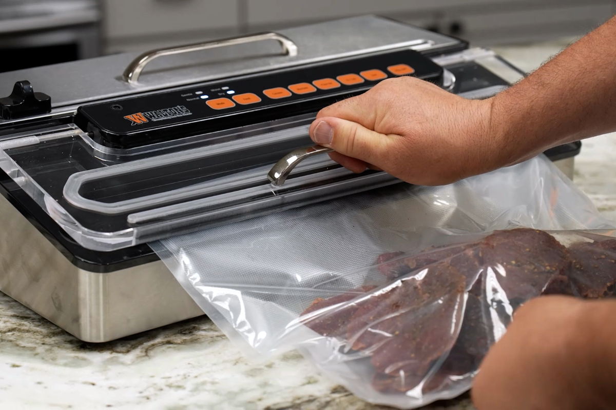 A person sealing meat in a vacuum sealer on a kitchen countertop.