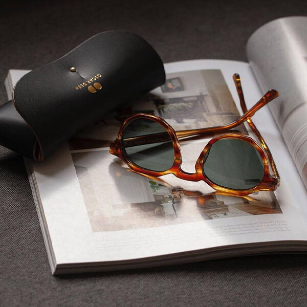 A lifestyle image of a pair of Oscar Deen Pinto sunglasses and case atop a magazine.