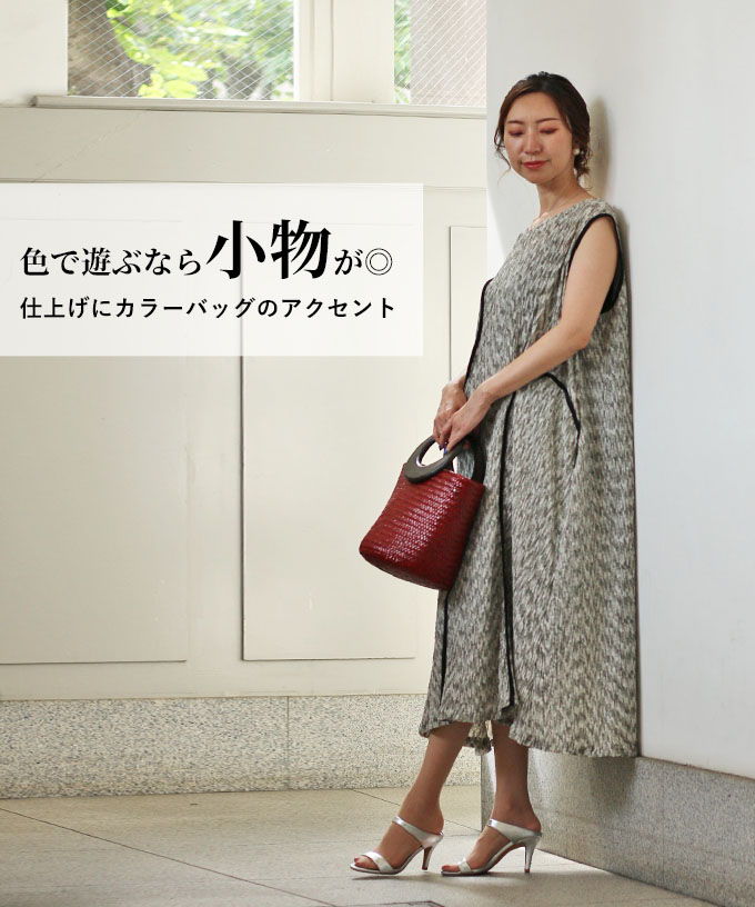 Woman in a stylish outfit holding a red handbag against a neutral background.