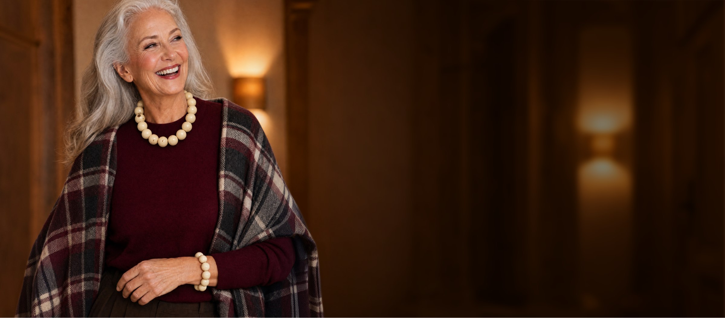 Smiling woman with long gray hair in a burgundy sweater and plaid wrap wearing a cream tagua bead necklace and bracelet