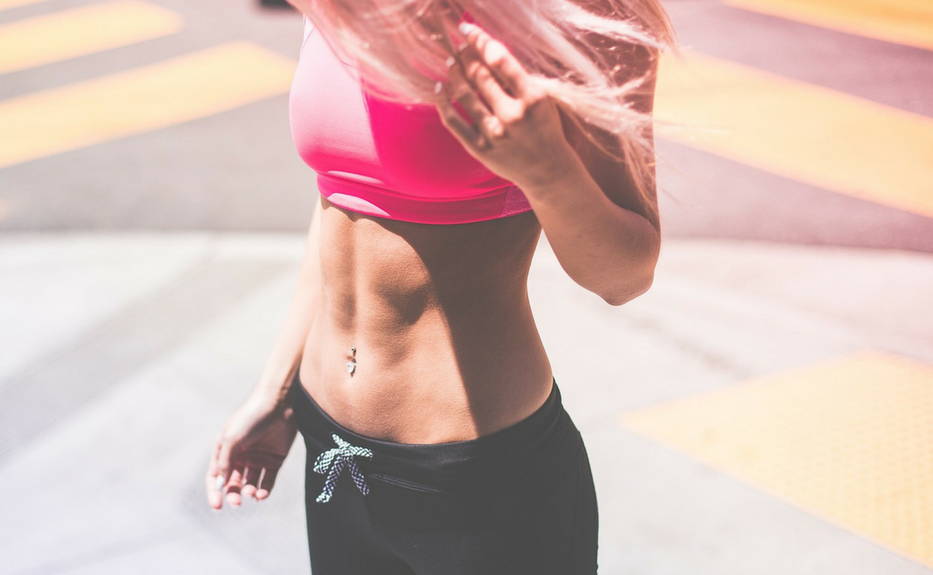 athlete standing in street, woman wearing pink sports bra and black yoga pants. She has blonde hair and is very fit.