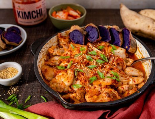 A bowl of spicy kimchi stew with purple sweet potatoes and garnished herbs.