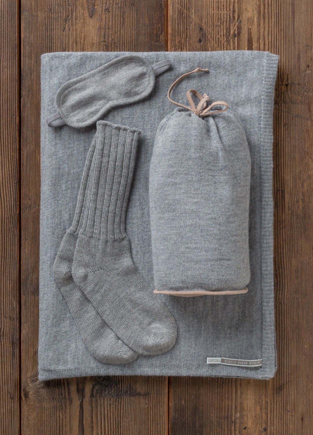 Cozy gray sleep set including blanket, socks, and eye mask on wooden background.