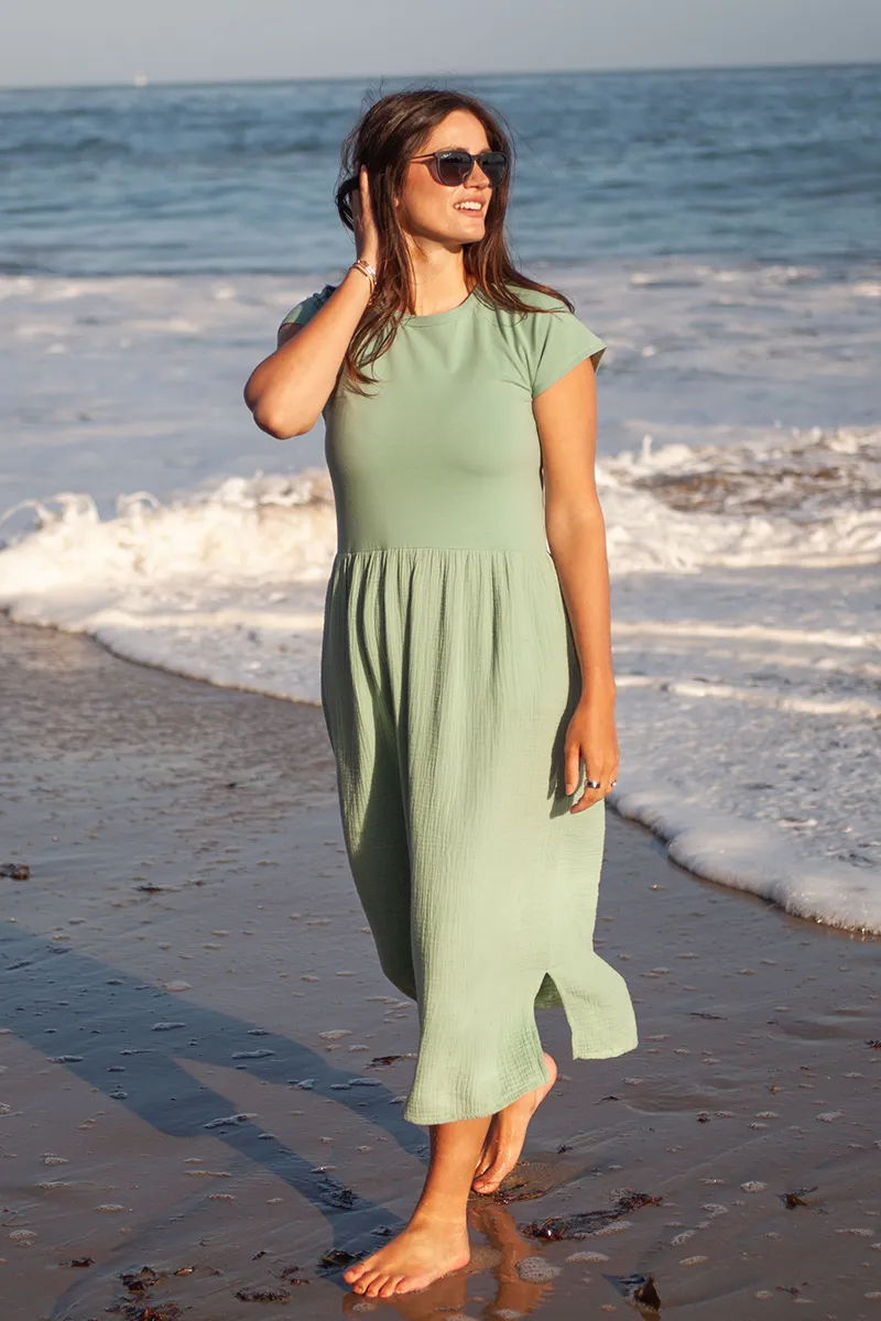 Woman in a green dress walking on the beach by the ocean.