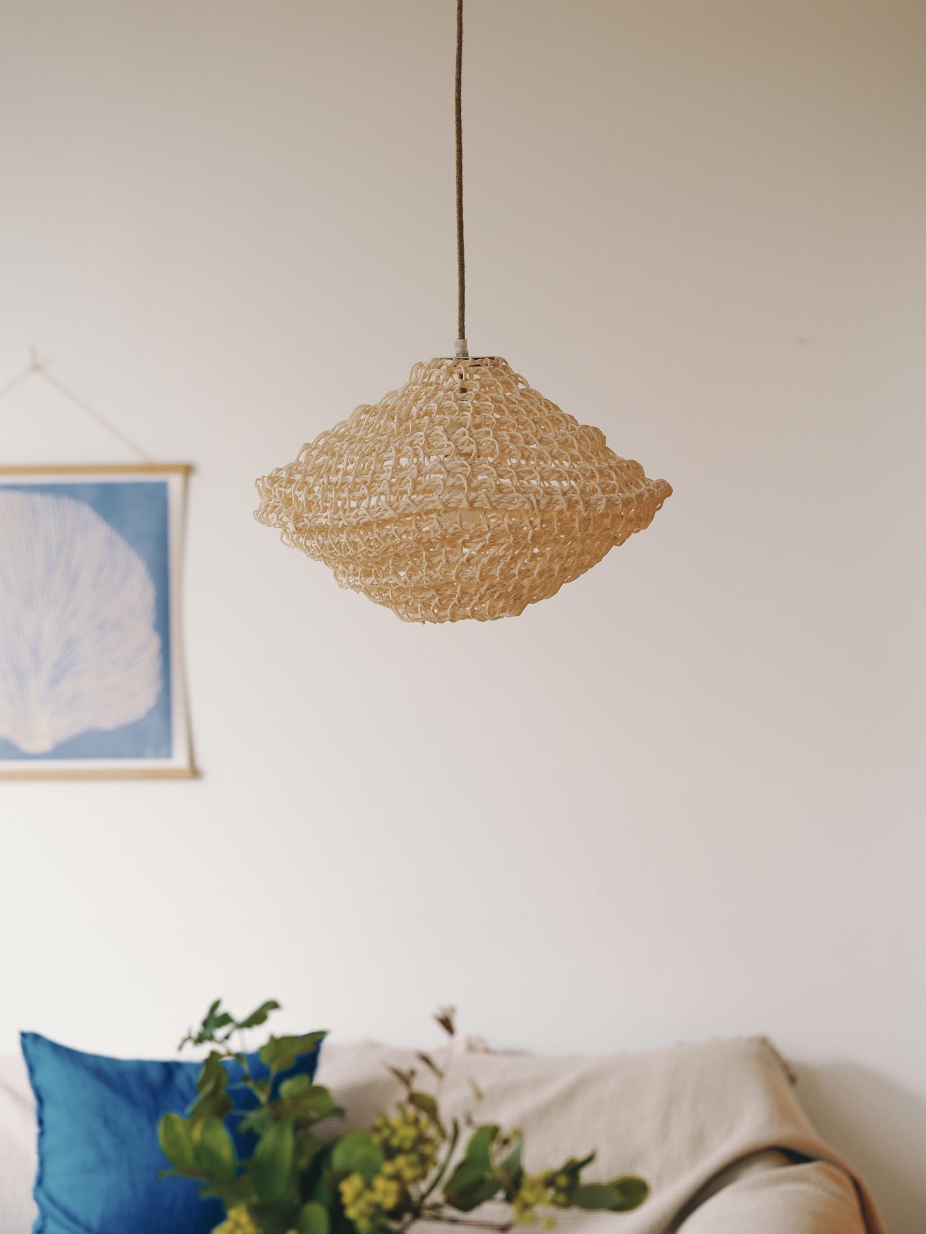 Woven pendant light hanging above a couch with decorative pillows and a plant.