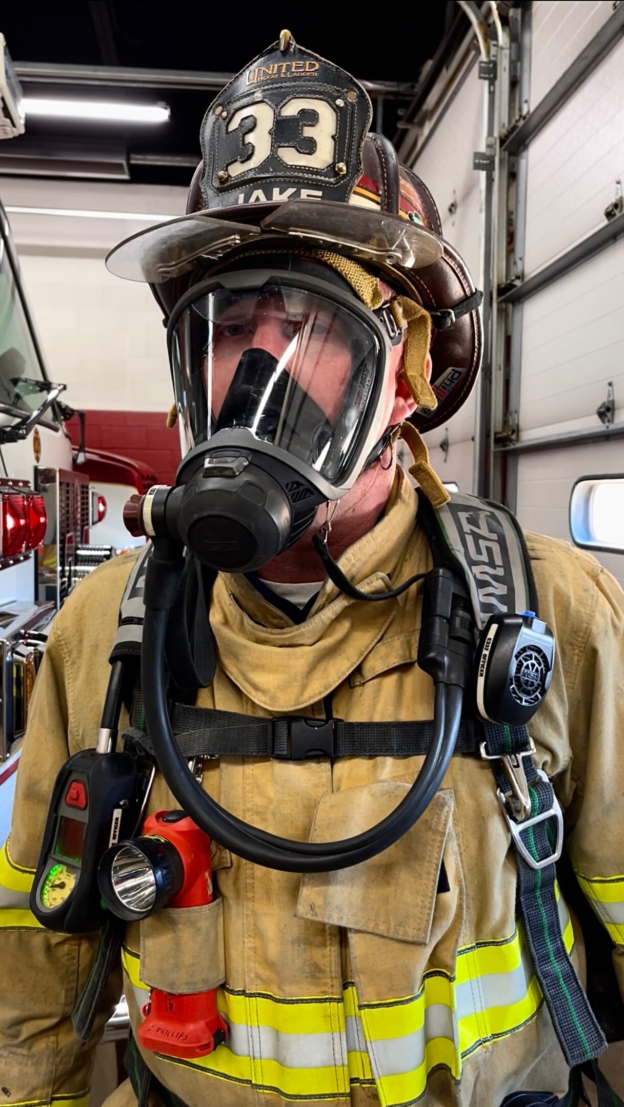 A firefighter wearing a helmet and mask, standing inside a fire station.