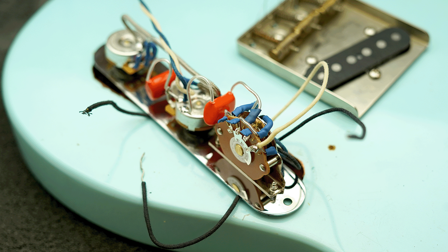 Close-up of guitar electronics and wiring on a light blue guitar body.