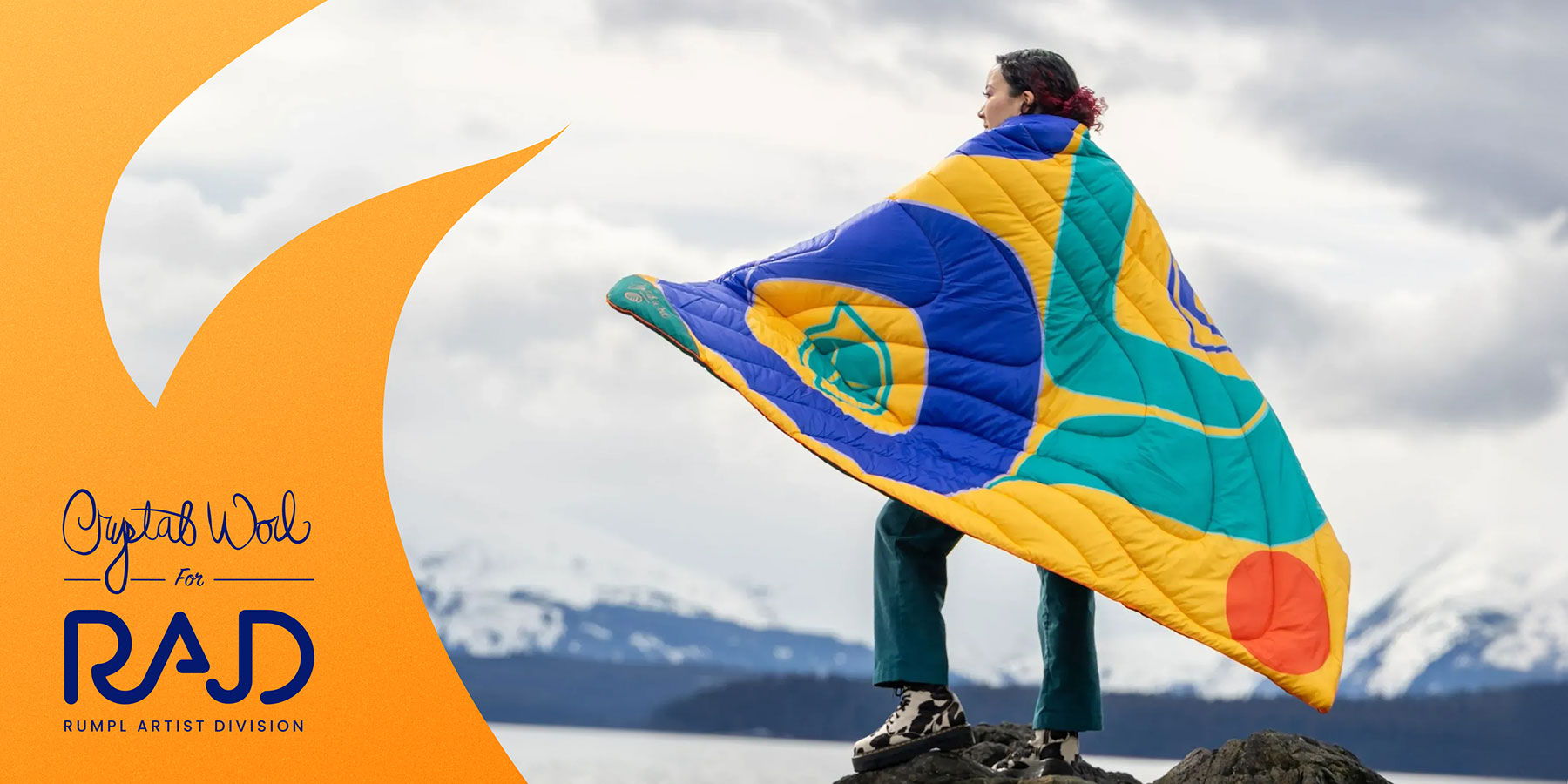 A person standing on a rock with a colorful blanket wrapped around their shoulders.