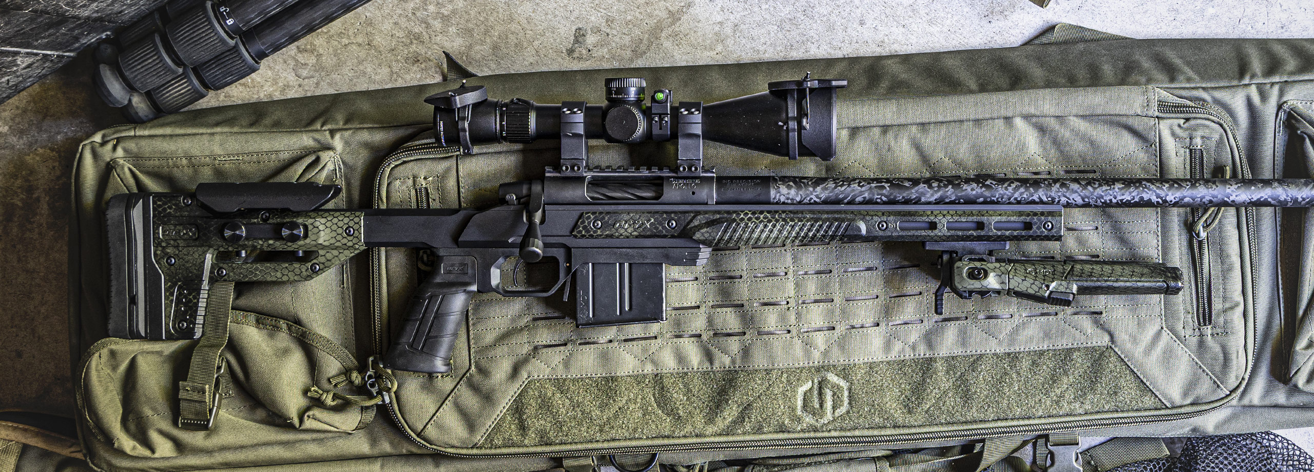 A black rifle with a scope on a green case.