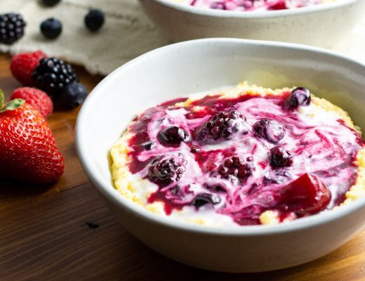 Bowl of yogurt topped with mixed berries and fruit sauce.