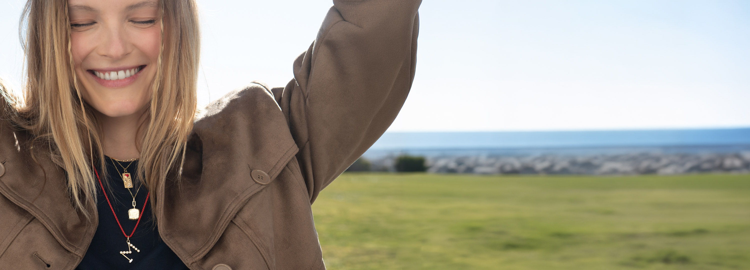 Smiling woman outdoors with arms raised, scenic background.