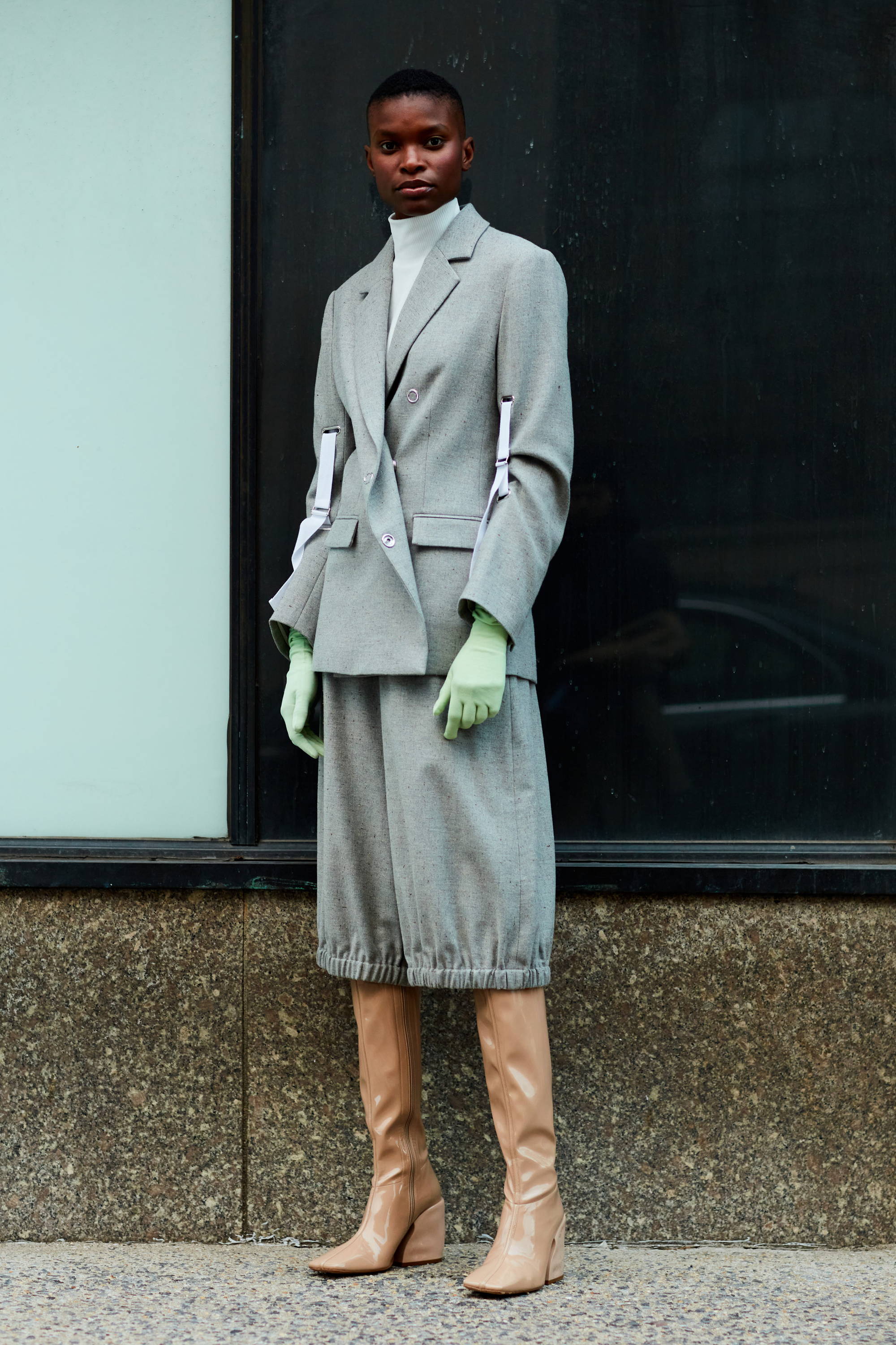 Person wearing a gray suit, green gloves, and beige boots on city street.