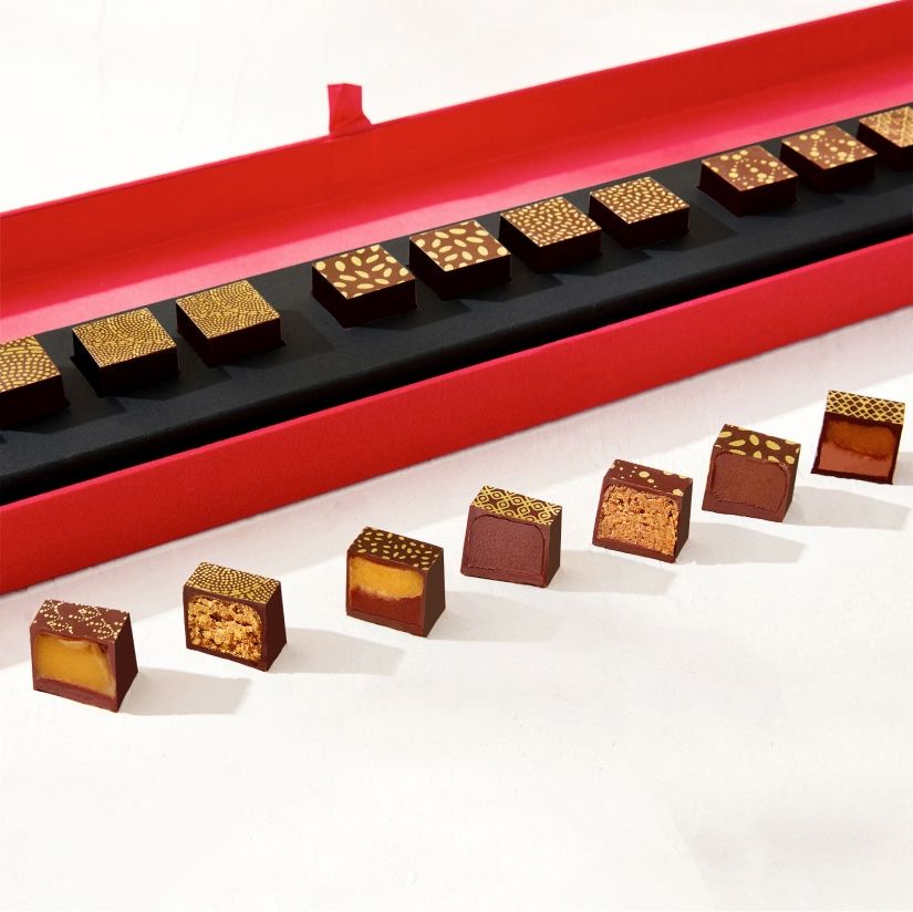 A hand reaching for chocolates on a red tray with flowers in the background.