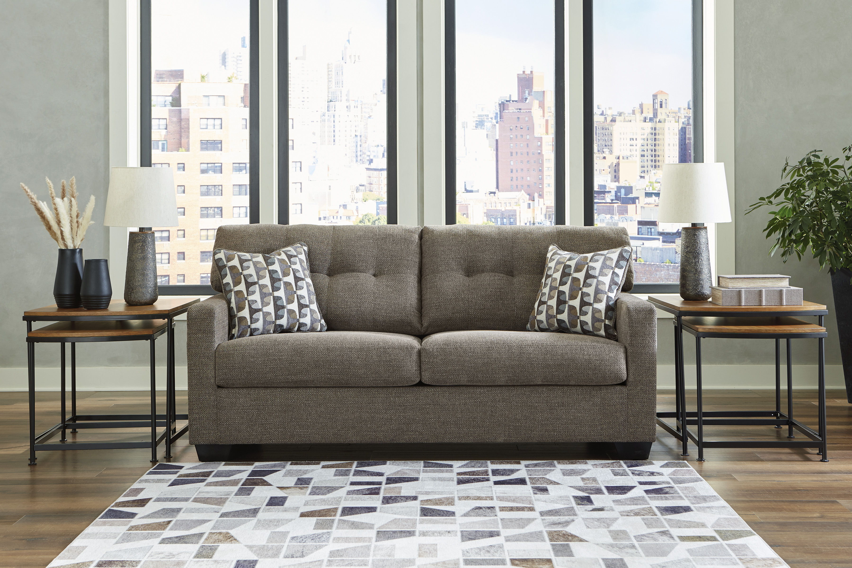 Brown sofa with decorative pillows, two side tables, and city view windows.