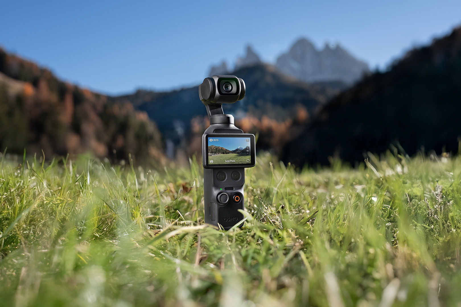 A DJI Osmo Action 4 camera in a grassy field with mountains in the background.