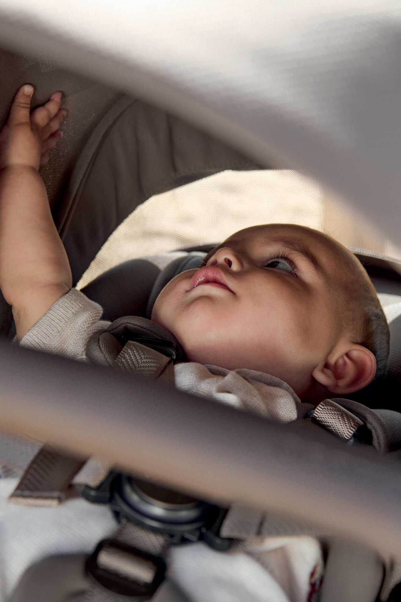Baby reaching up while sitting in a stroller.