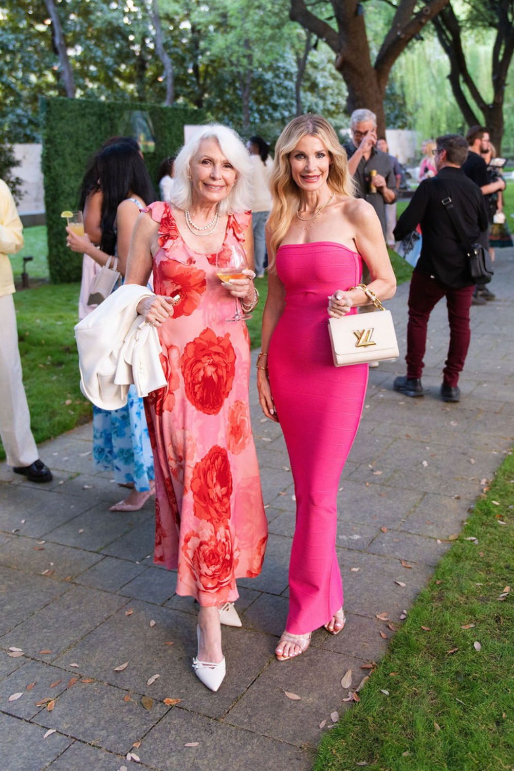 Two women walking together at a social event in a garden.