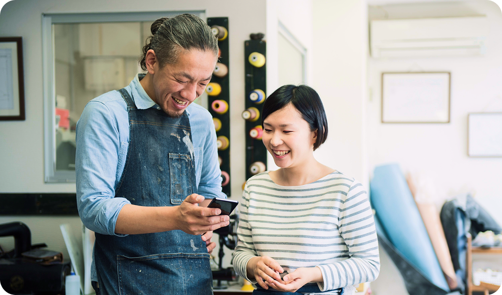 Two people smiling and looking at a smartphone in a cozy setting.