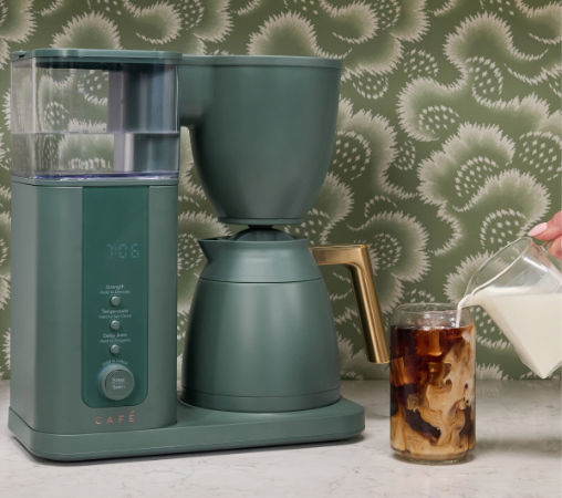 Coffee maker next to a glass of iced coffee with milk being poured.