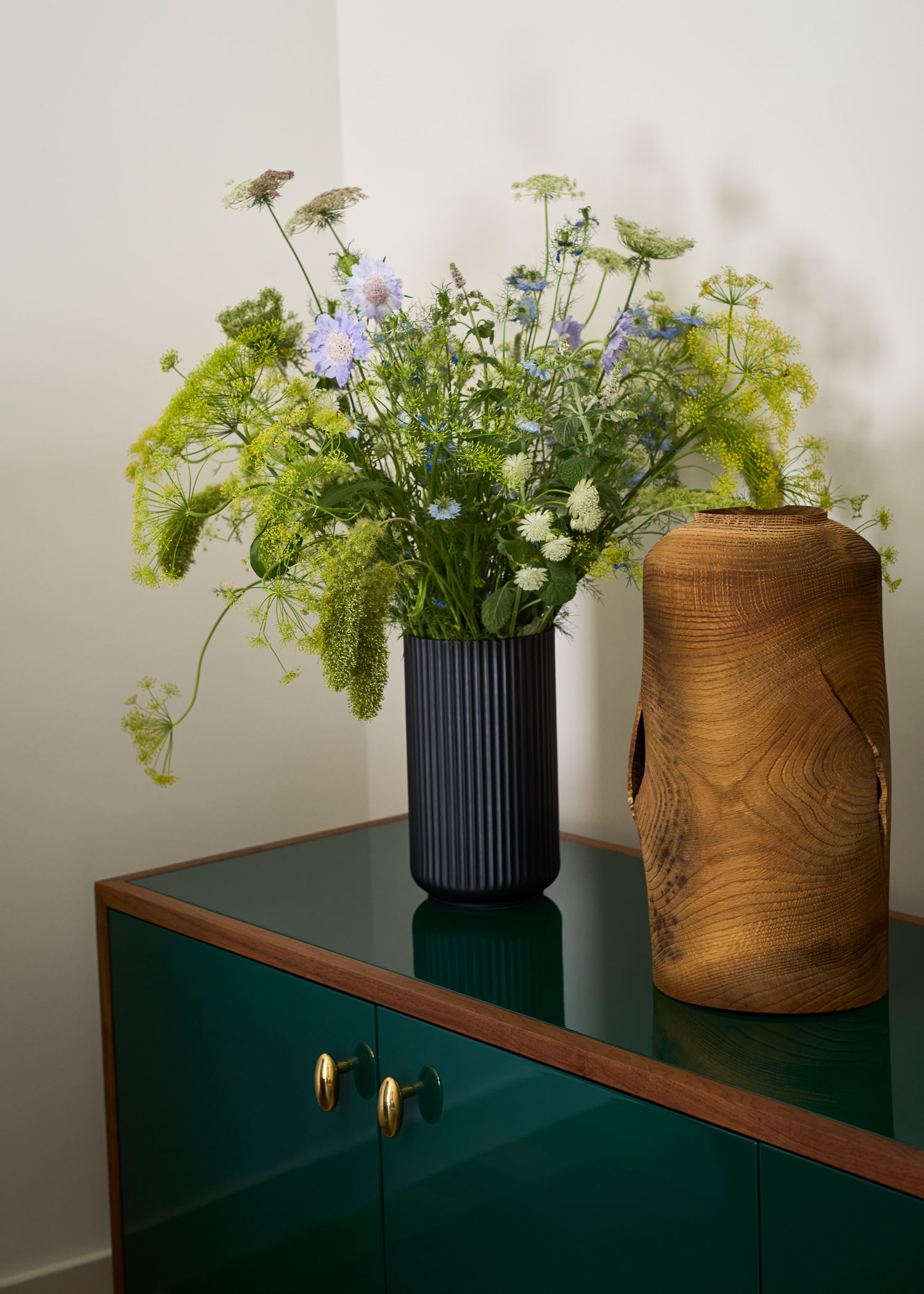 A vase with flowers next to a wooden decorative object on a green table.