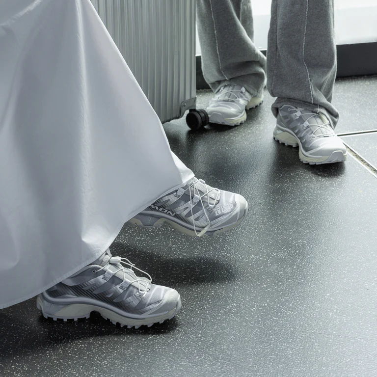 Two pairs of feet in sneakers on a dark floor.