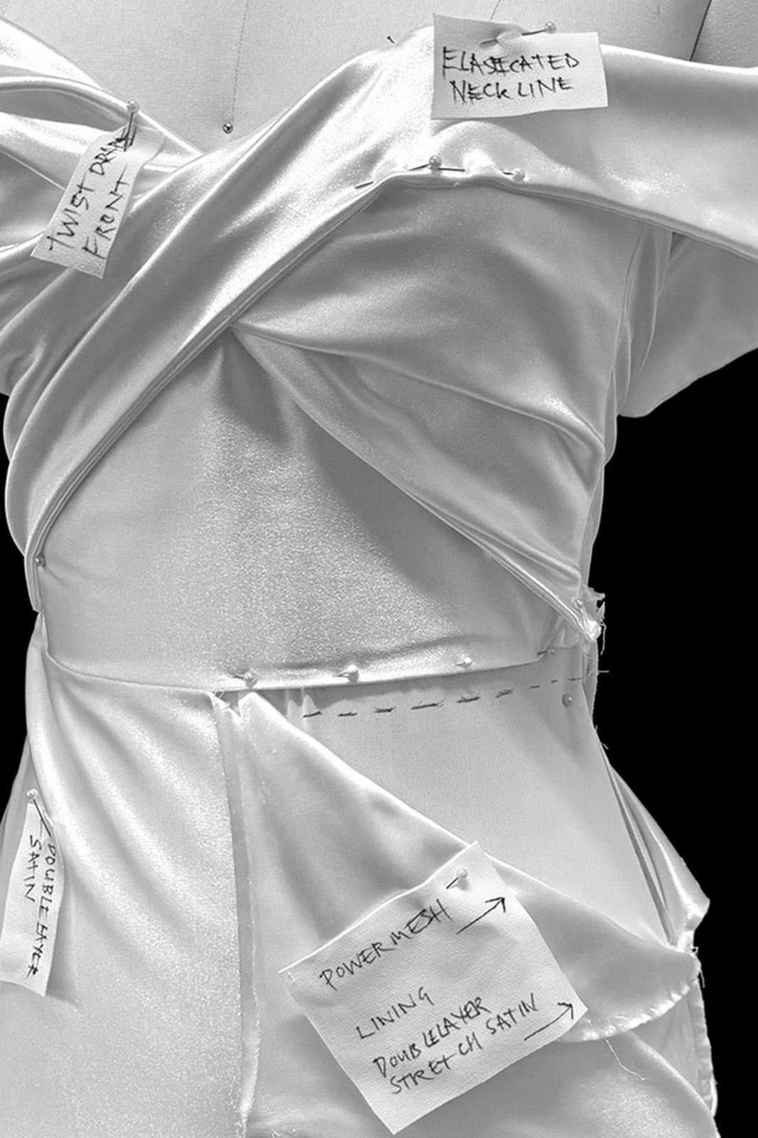 Close-up of draped fabric with handwritten labels and notes on a dress form.