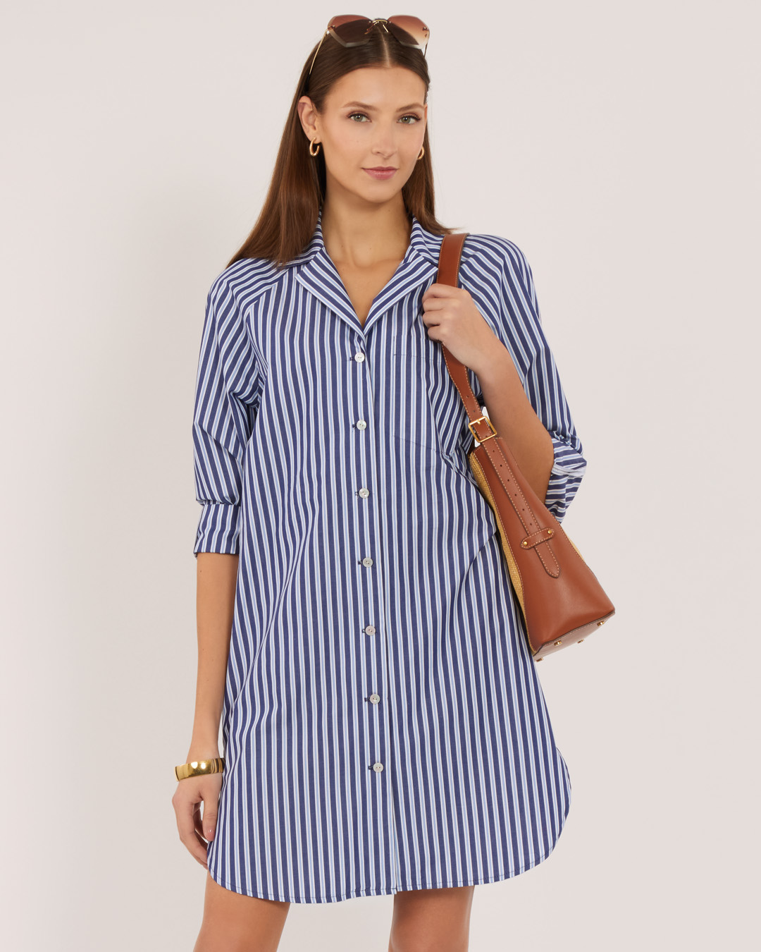 Woman in a striped dress holding a brown handbag.