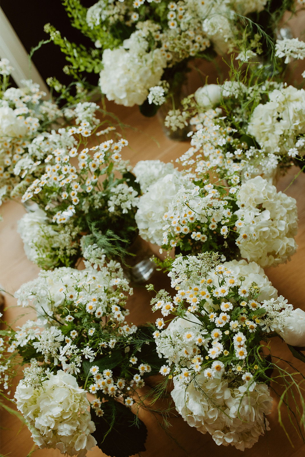 Bunches of white flowers arranged in vases on a wooden table.