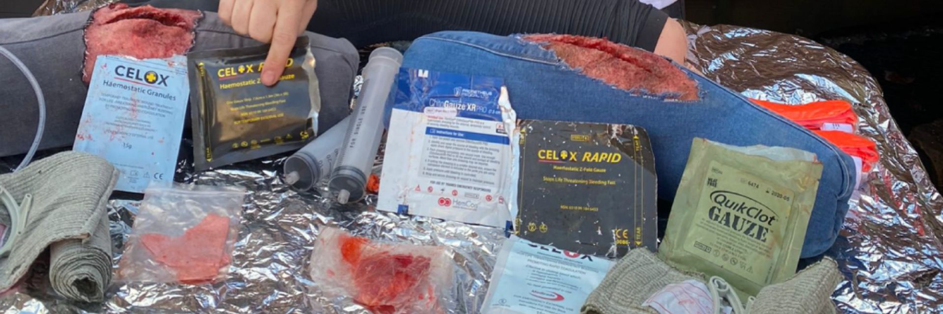 First aid supplies arranged on a blanket, with a hand pointing at them.