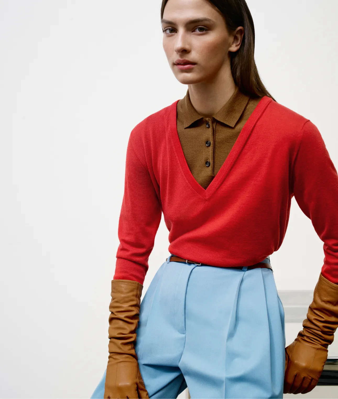 Model wearing a red sweater and blue pants with brown gloves.