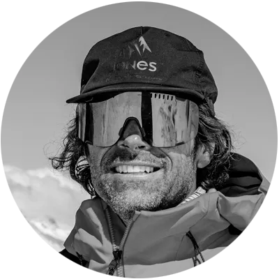 Man wearing a hat and sunglasses, smiling against a mountainous background.