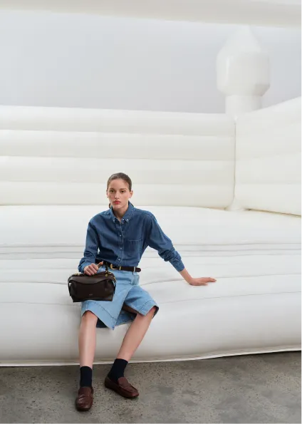 Woman sitting on an inflatable white structure, wearing a denim shirt and skirt.