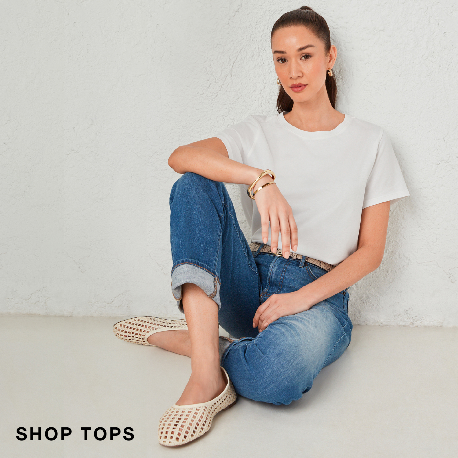 Woman sitting in casual outfit, featuring a white t-shirt and blue jeans.
