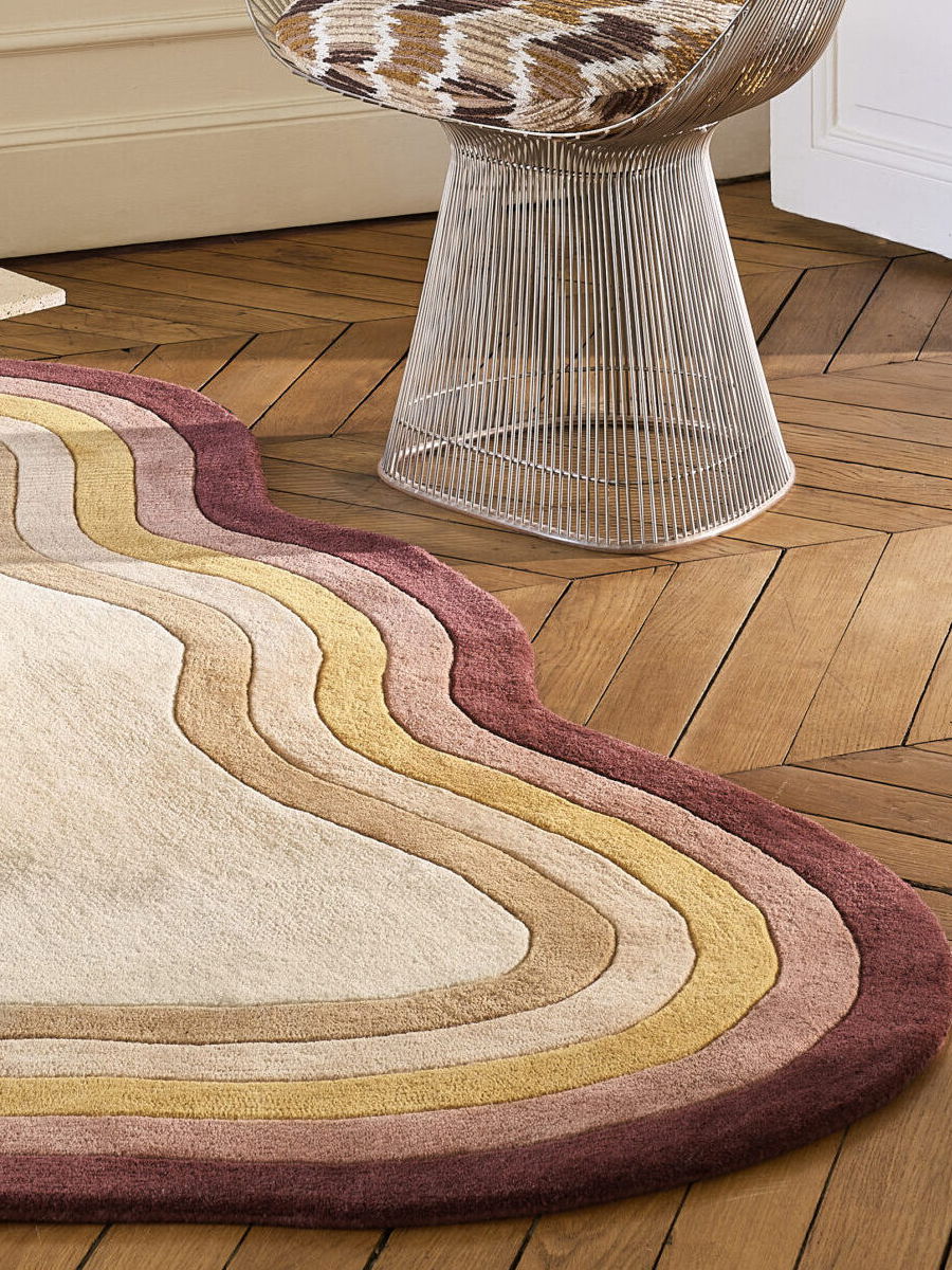 Colorful rug with wavy stripes next to a modern chair on wooden floor.
