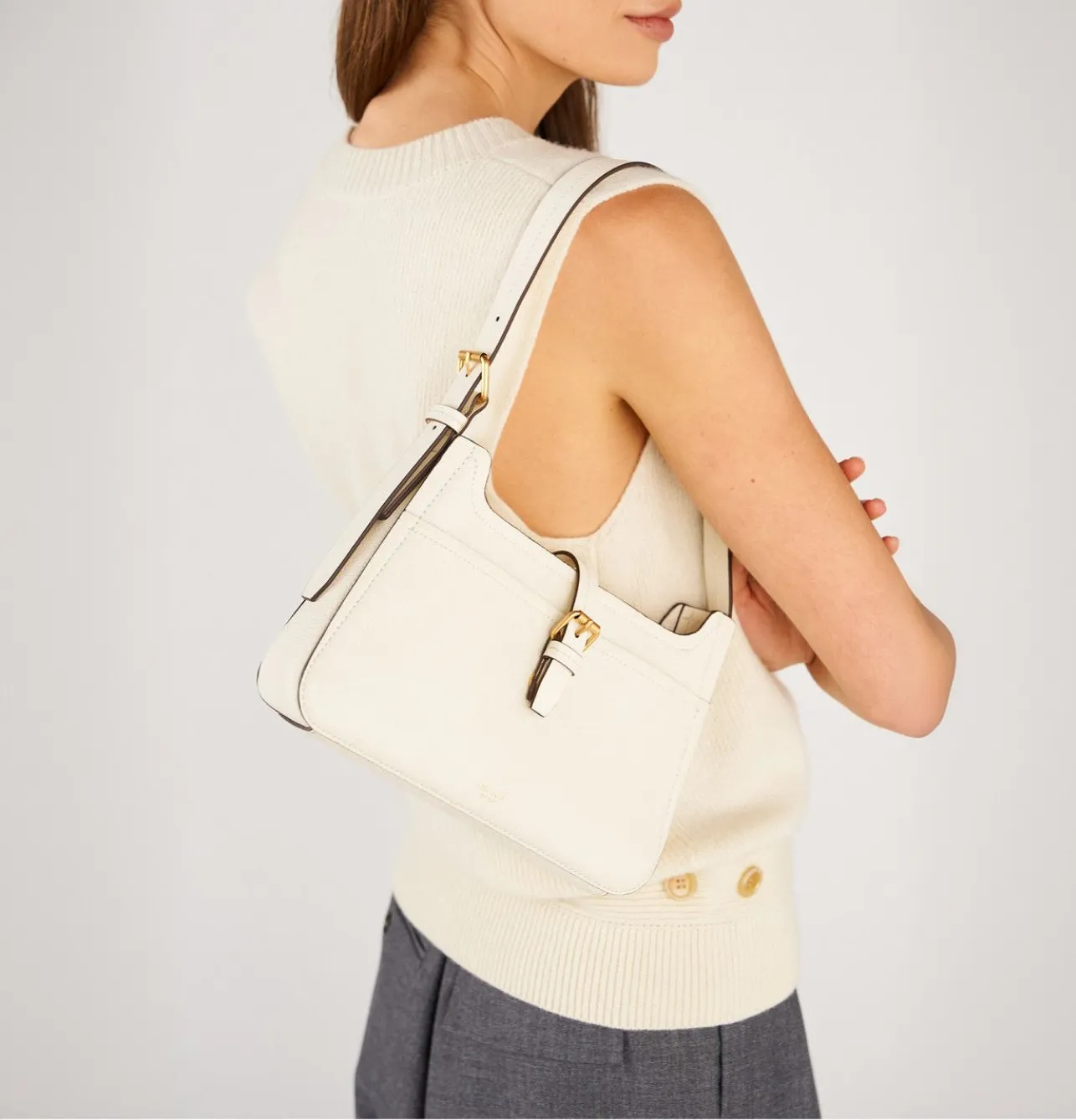 Woman wearing a sleeveless sweater holding a white handbag.