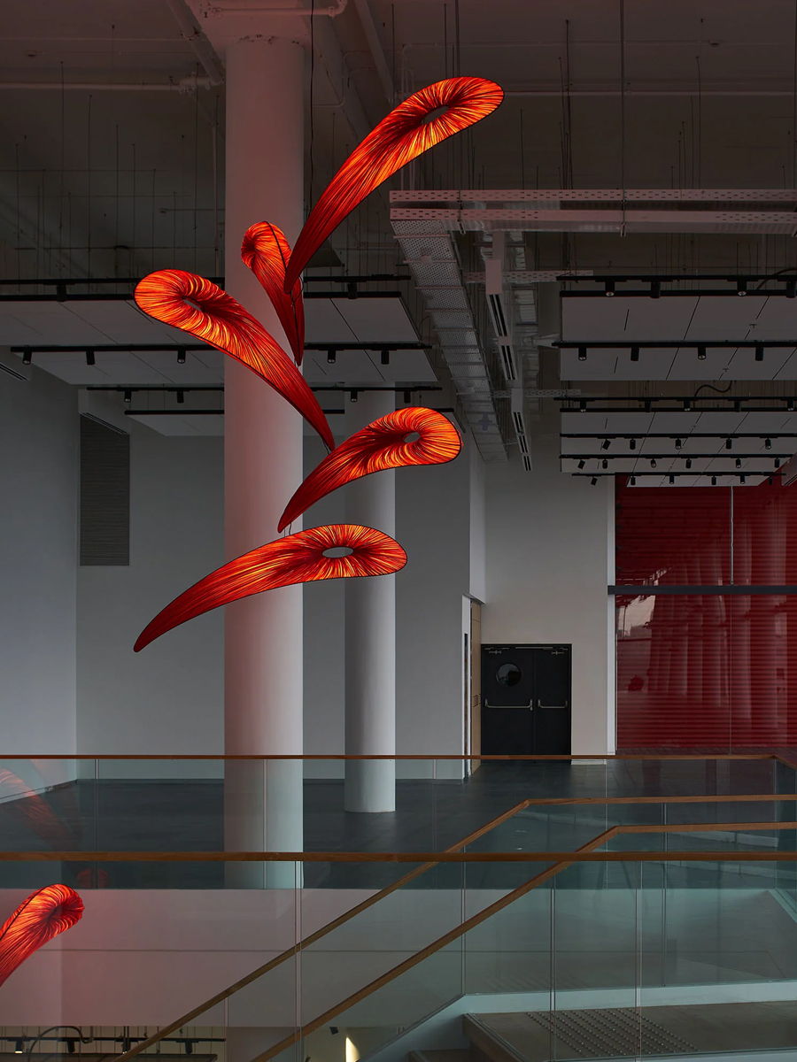 Red abstract lighting sculptures hanging in a modern, spacious gallery.