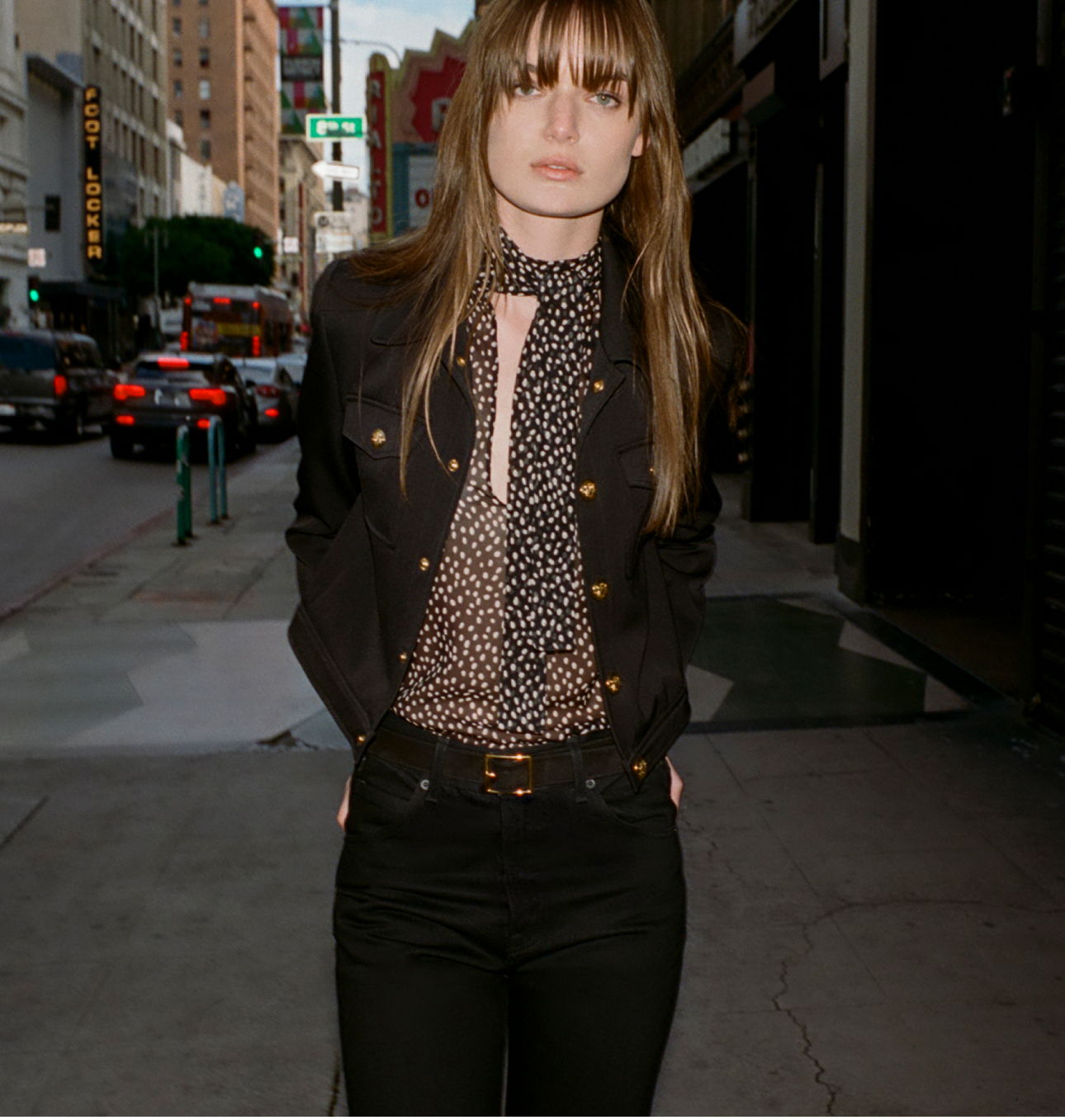A woman in a black outfit stands on a city street.