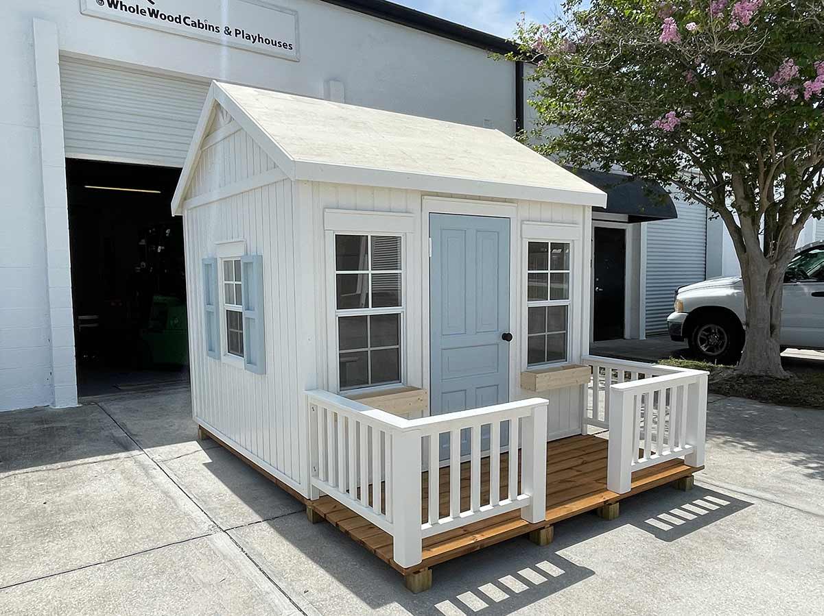 Farmhouse Style Outdoor Playhouse with natural Flower boxes and blue door and window shutters and wooden terrace with white railings by WholeWoodPlayhouses