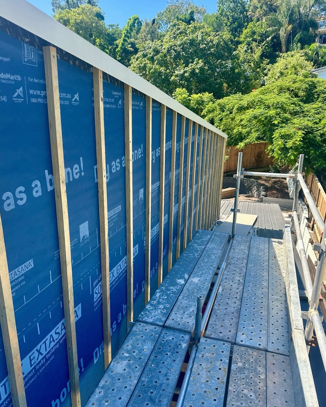 Construction site with framed wall and blue sheathing material.